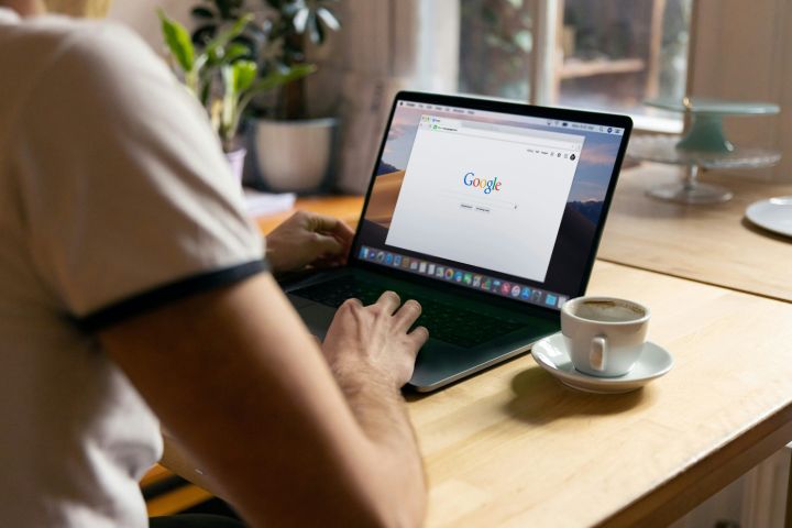 Person verwendet Google auf Laptop neben Kaffeetasse.